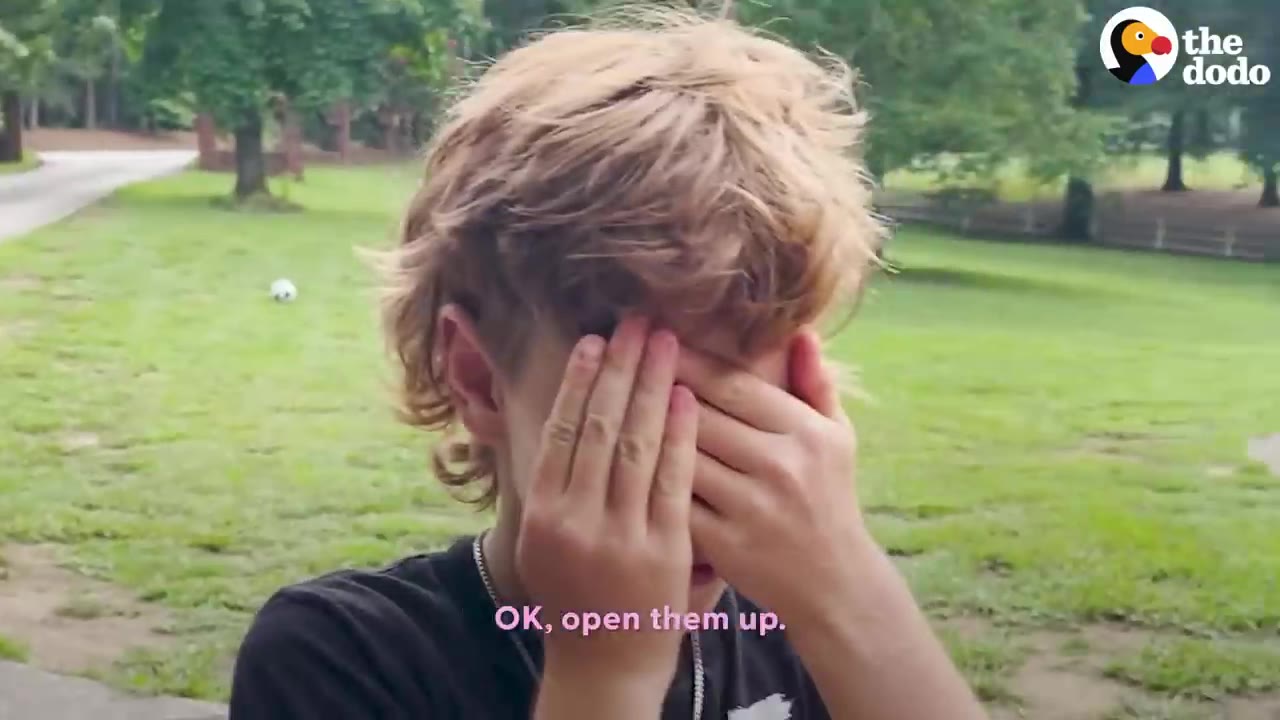 A young person covering their eyes with their hands outdoors on a lawn.