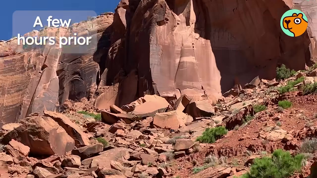 A wide view of a rugged red rock canyon landscape with scattered boulders and desert vegetation.