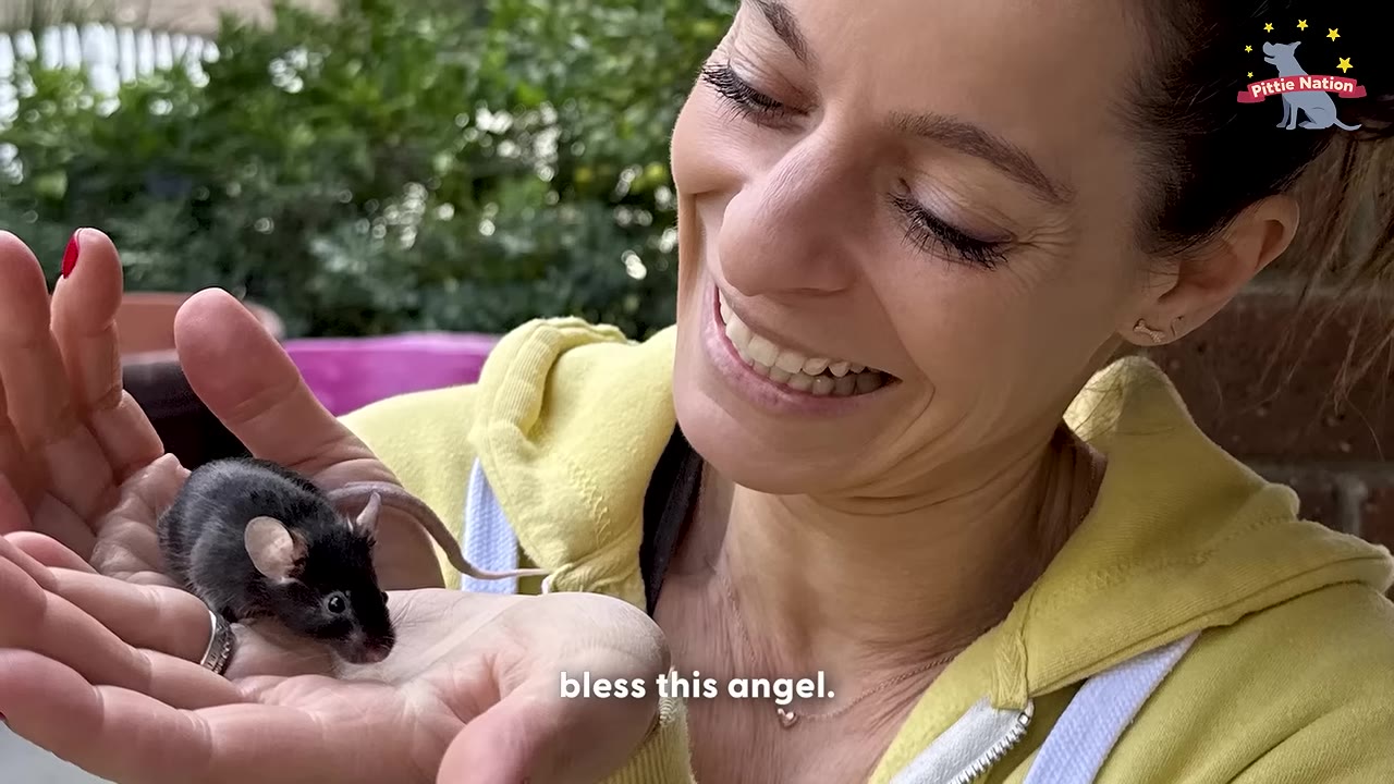 A smiling woman holding a tiny black mouse in the palm of her hand.