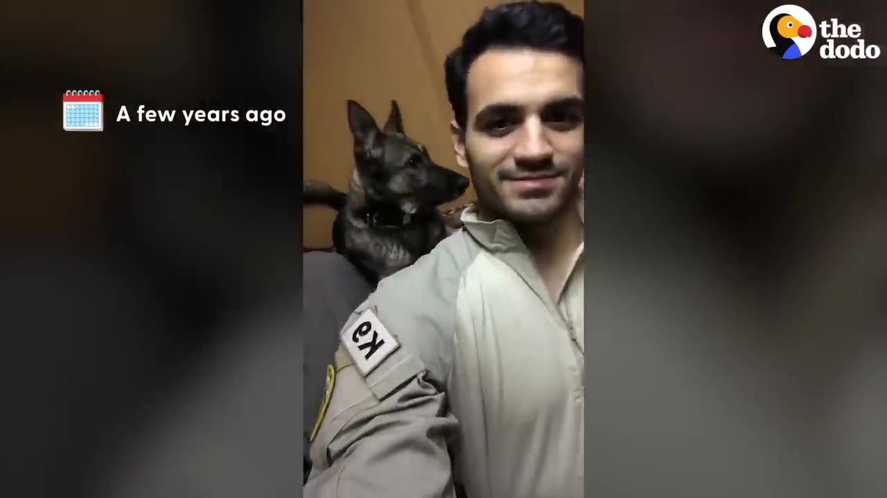 A smiling military handler in uniform takes a selfie with a German Shepherd working dog behind him.