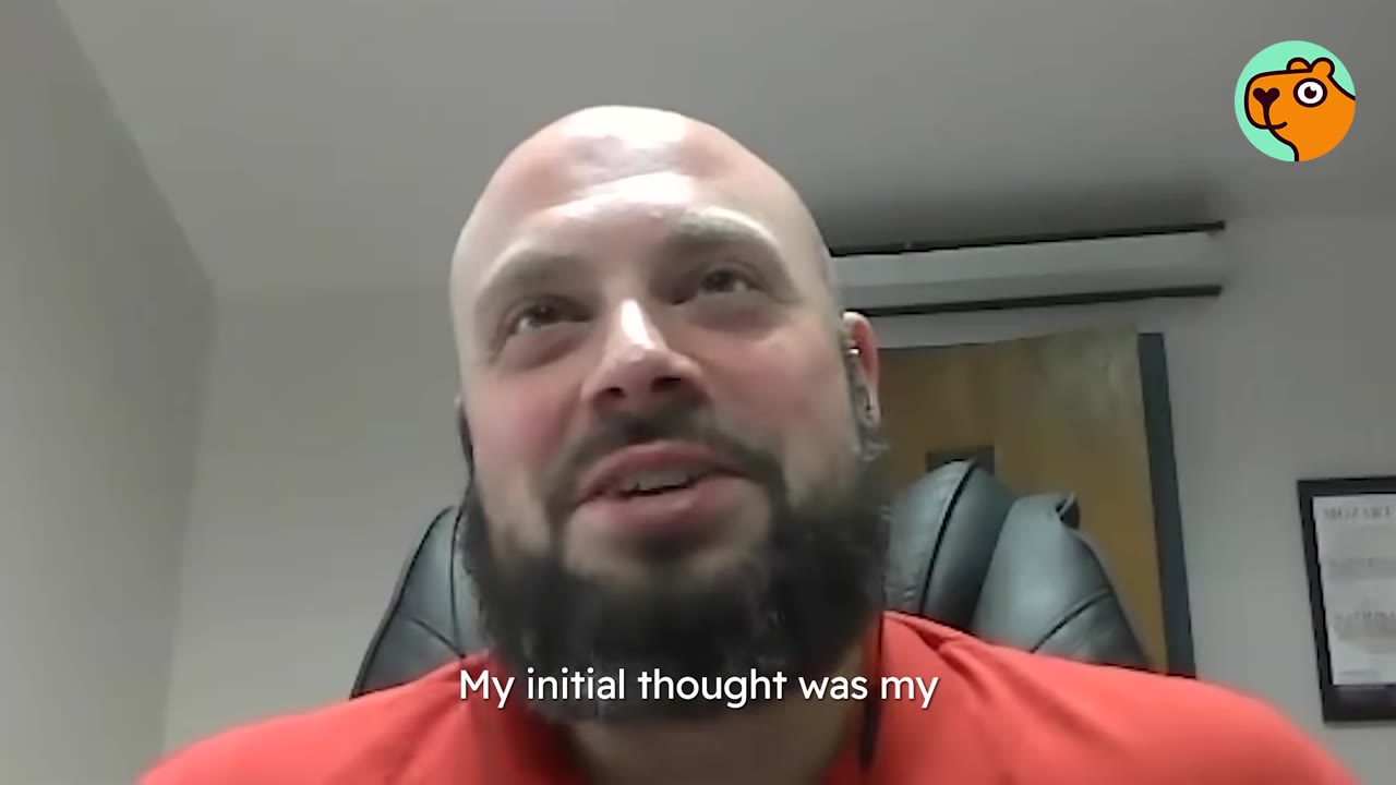 A close-up view of a bald man with a beard talking in an office setting.