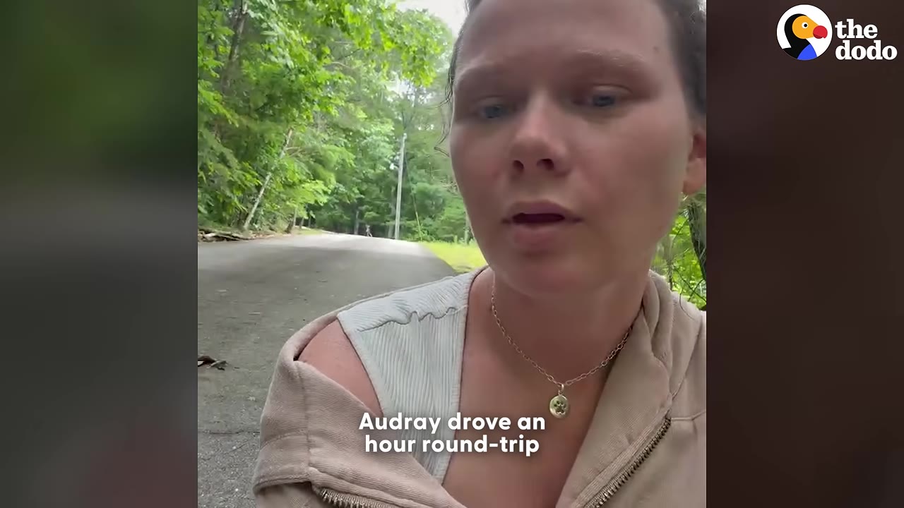 A close-up shot of a woman named Audray speaking to the camera, with a paved road and green trees in the background.