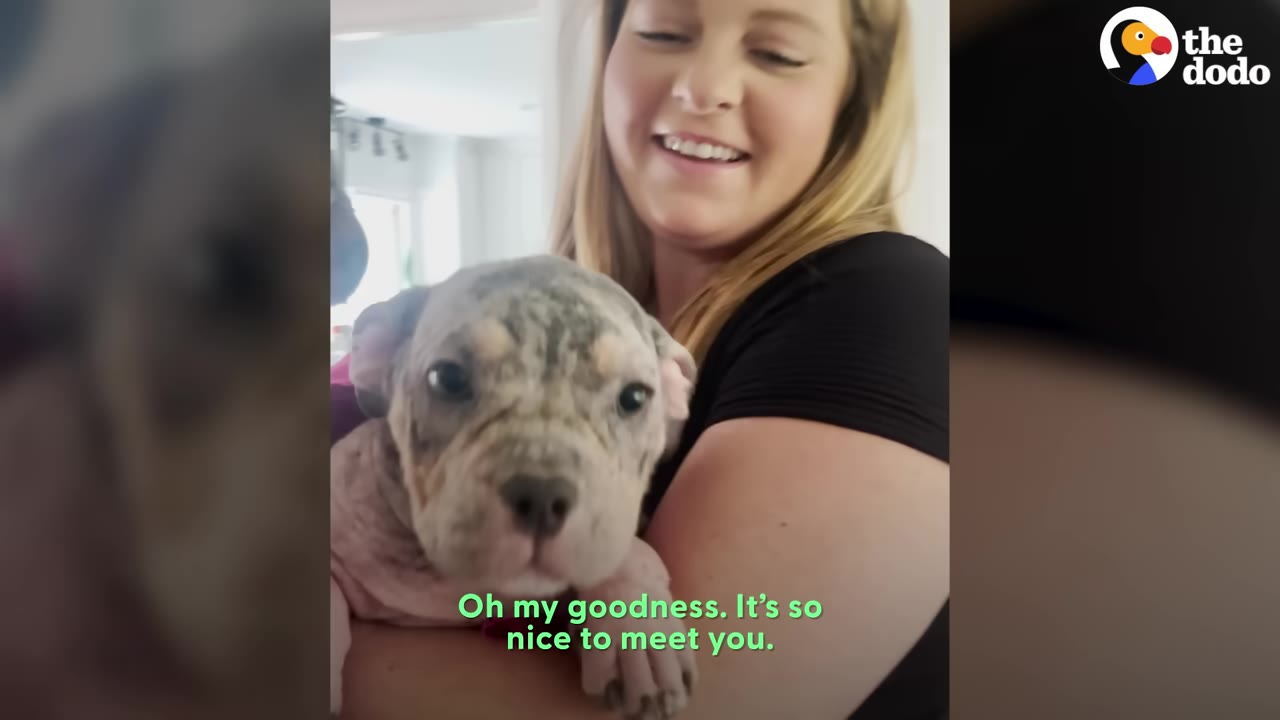 A smiling woman holding a small speckled puppy with skin issues close to her chest.