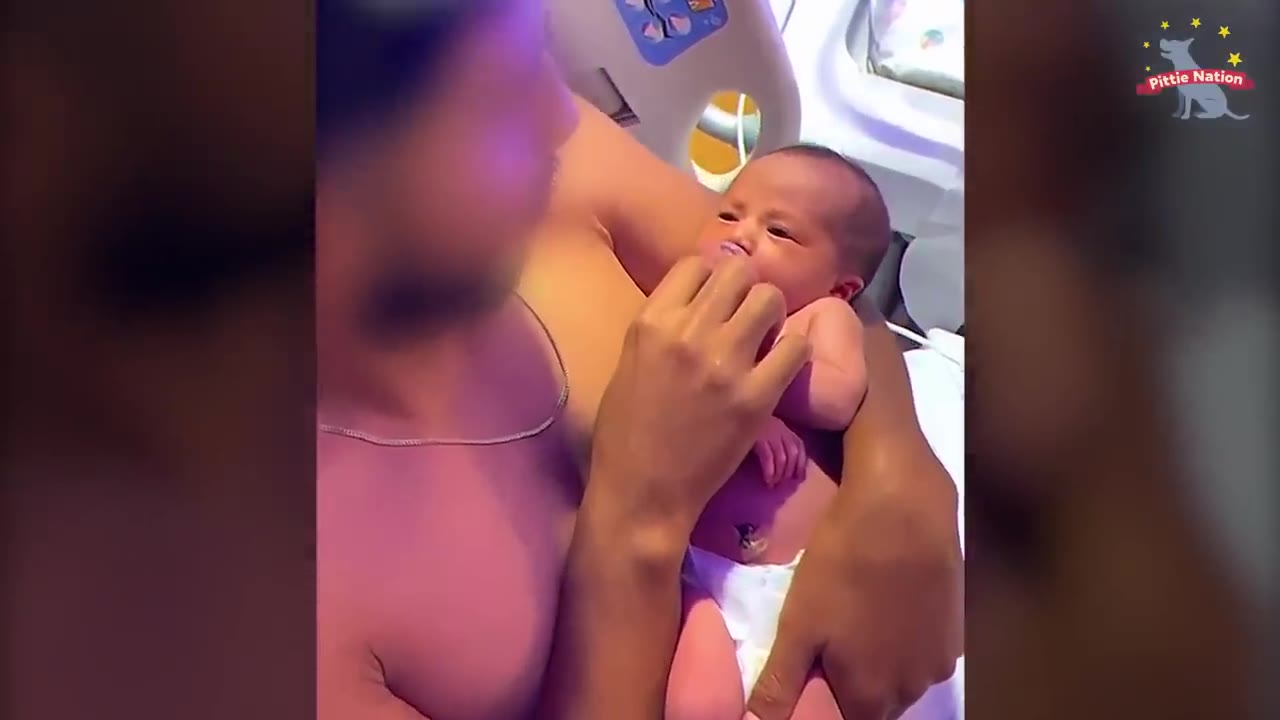 A newborn baby girl in a diaper is held close by a parent in a hospital setting.