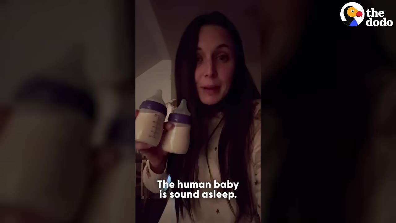 A woman with long dark hair holds up two baby bottles filled with milk in a dimly lit room at night.