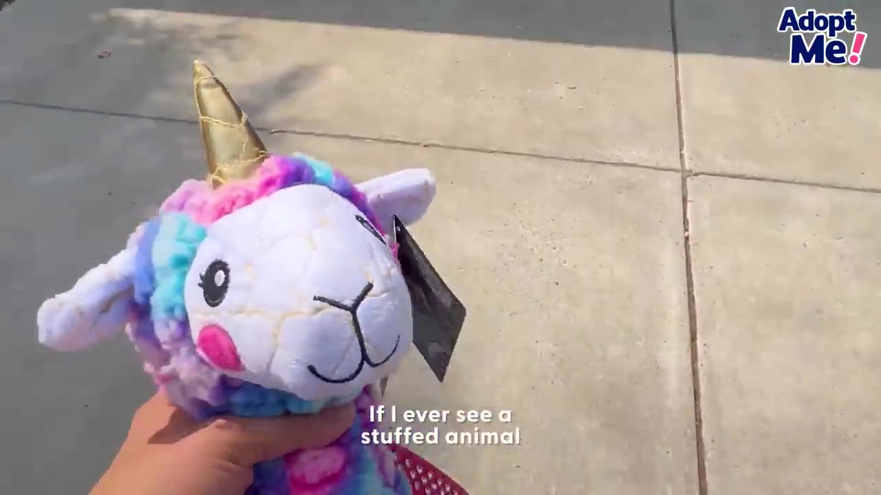 A hand holding up a colorful plush unicorn toy with a gold horn outdoors.