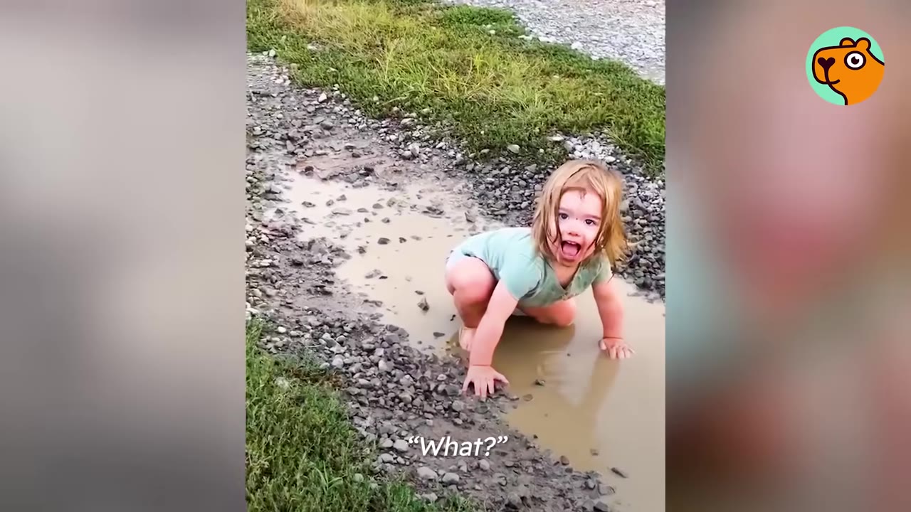 A toddler crouching on all fours in a muddy puddle outdoors while looking up at the camera.