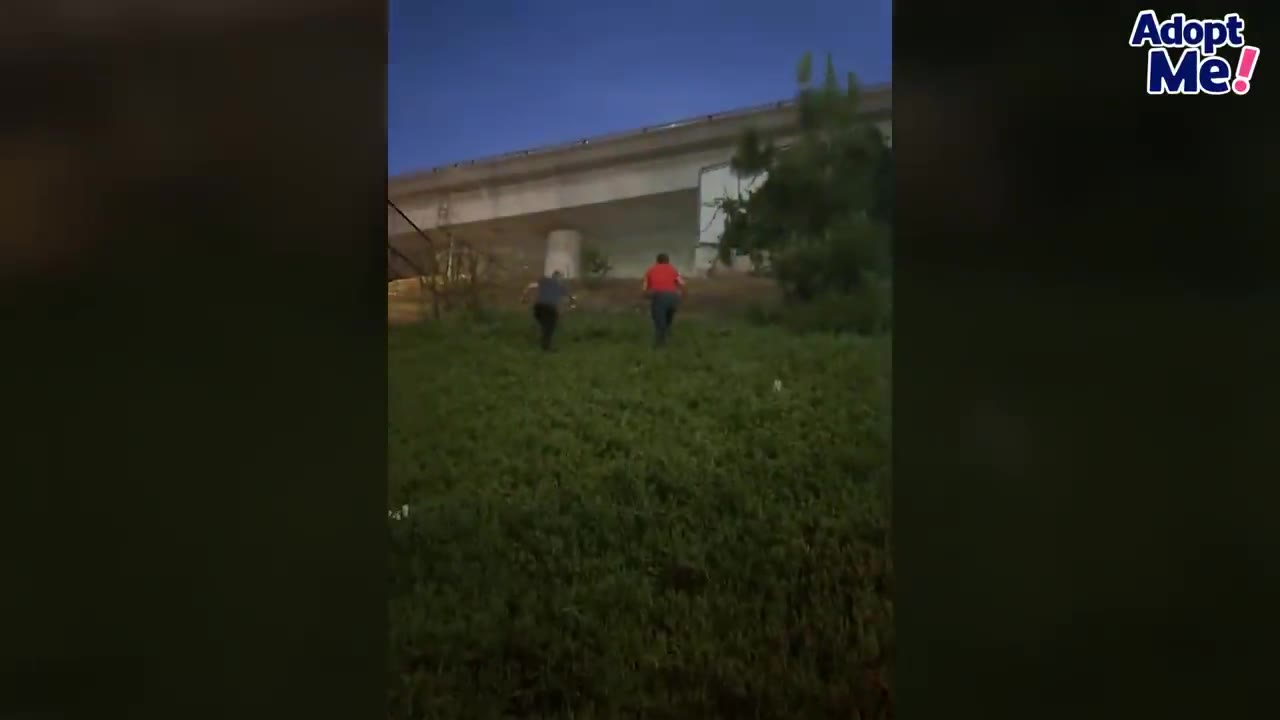 Two people running up a grassy hill towards an overpass at dusk.