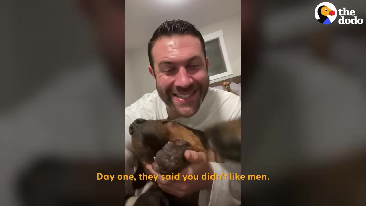 A smiling man holding a brown dog close to his face indoors.