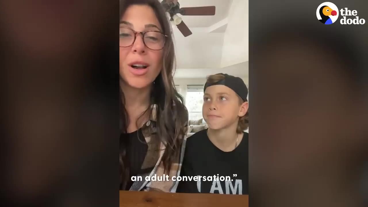 A woman wearing glasses talking while a young boy wearing a backward cap looks at her attentively.