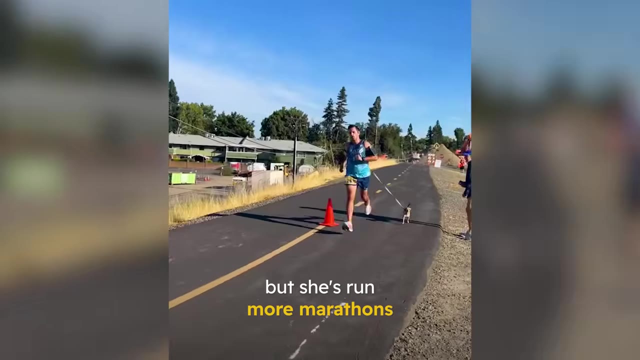 A man running down a paved road during a marathon with a small dog running beside him on a leash.