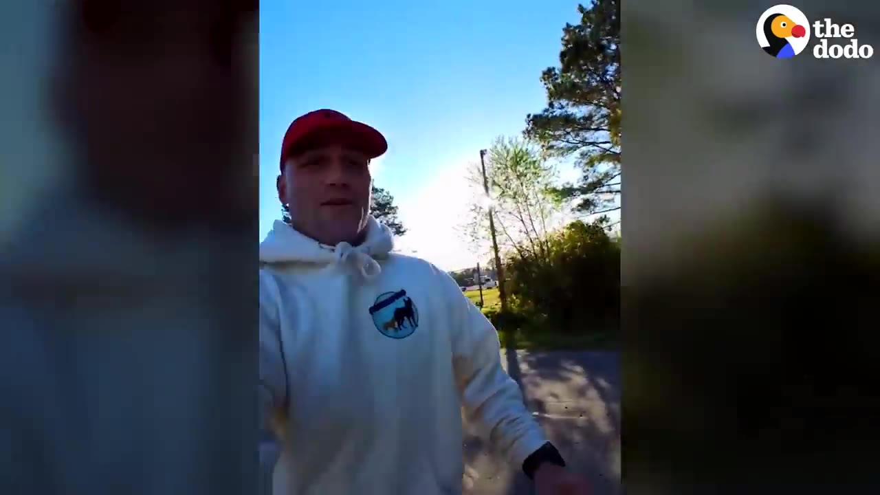 A man wearing a red cap and a white hoodie walking outside on a sunny day.