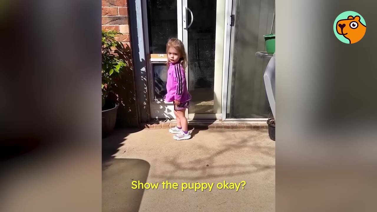 A young child wearing a purple jacket standing near a sliding glass patio door outside.
